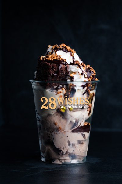 A clear 28 Wishes cup layered with ice cream, topped with a brownie, whipped cream, chocolate drizzle and crunchy pieces